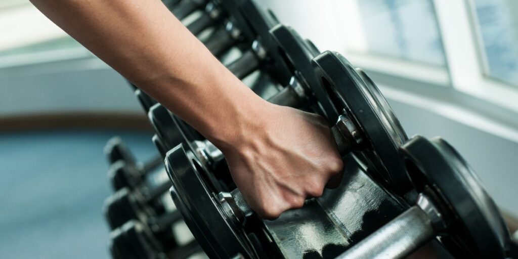 A person's arm reaching out to select a dumbbell from a rack in a gym.
