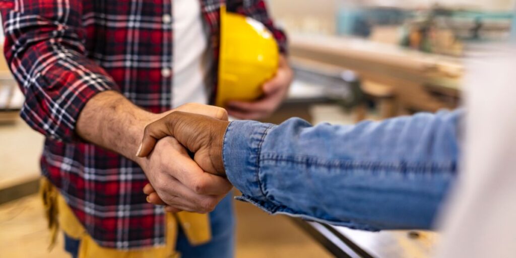 Close-up of a handshake between a contractor wearing a plaid shirt and a client in a blue denim shirt.