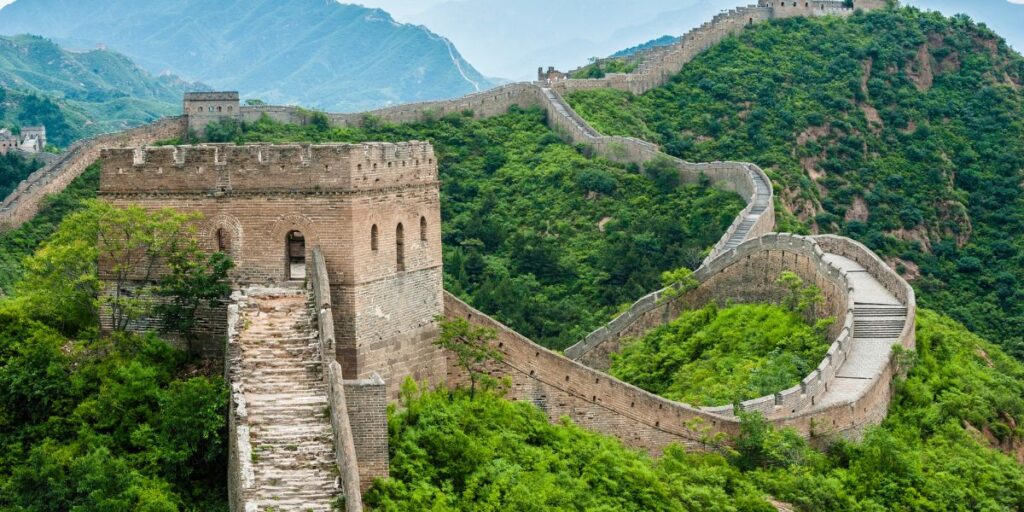 The serpentine path of the Great Wall of China winds through lush greenery and rugged terrain, showcasing the grandeur of ancient fortifications.
