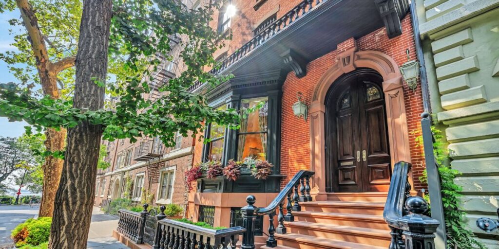 A classic brownstone townhouse with a stoop and ornate doorway surrounded by lush greenery.