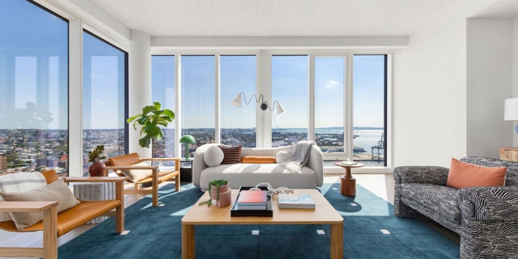 A bright and spacious living room with floor-to-ceiling windows offering a panoramic city view.