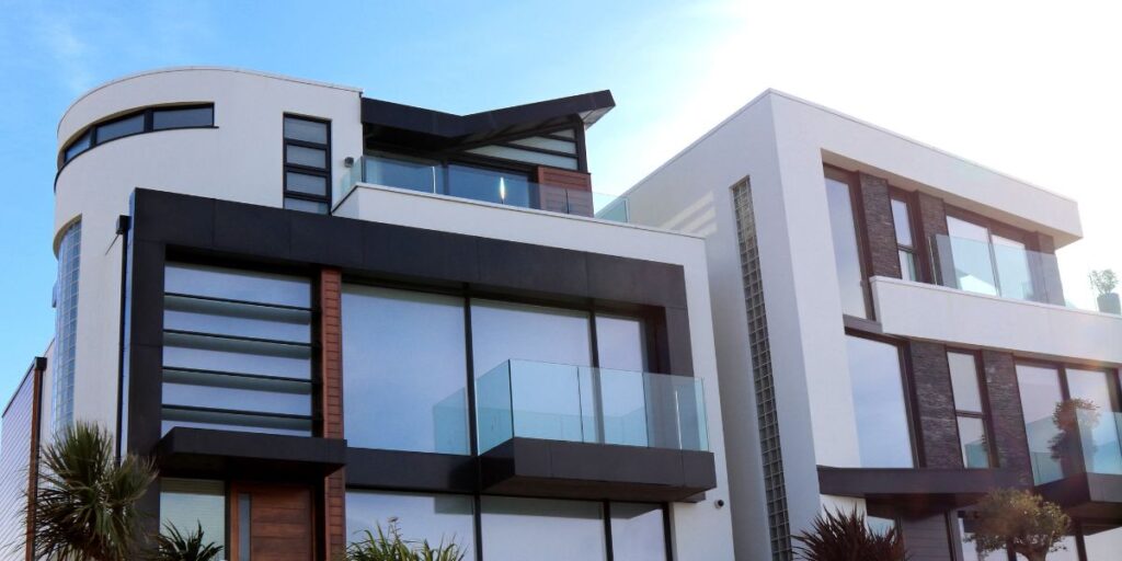 Two modern homes with flat roofs, white and black exteriors, large windows, and balconies with glass railings.