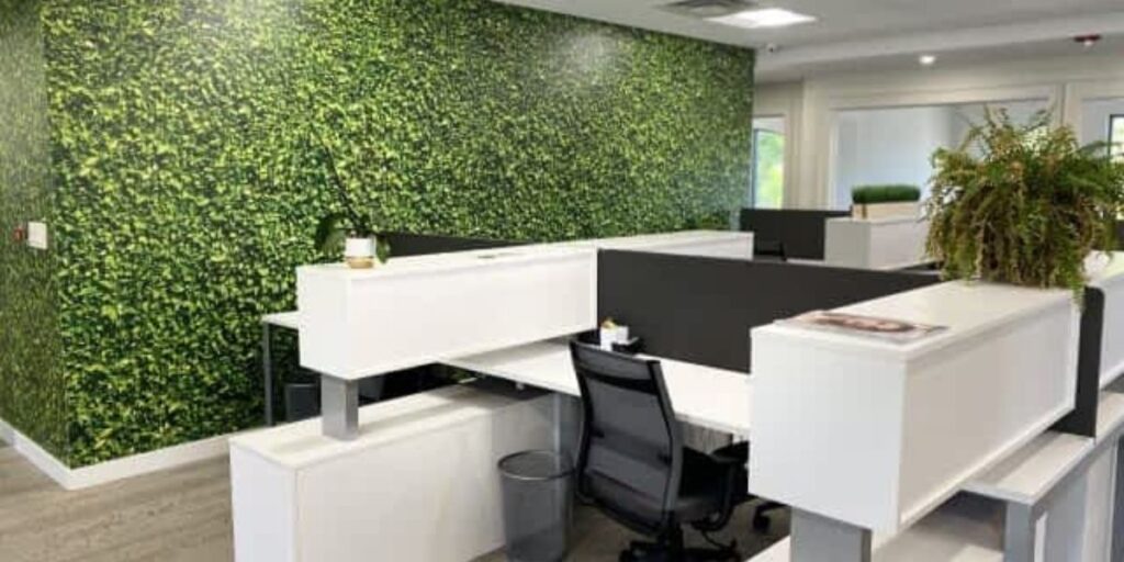 Modern office cubicles with white desks, black partitions, and a vibrant green living wall.