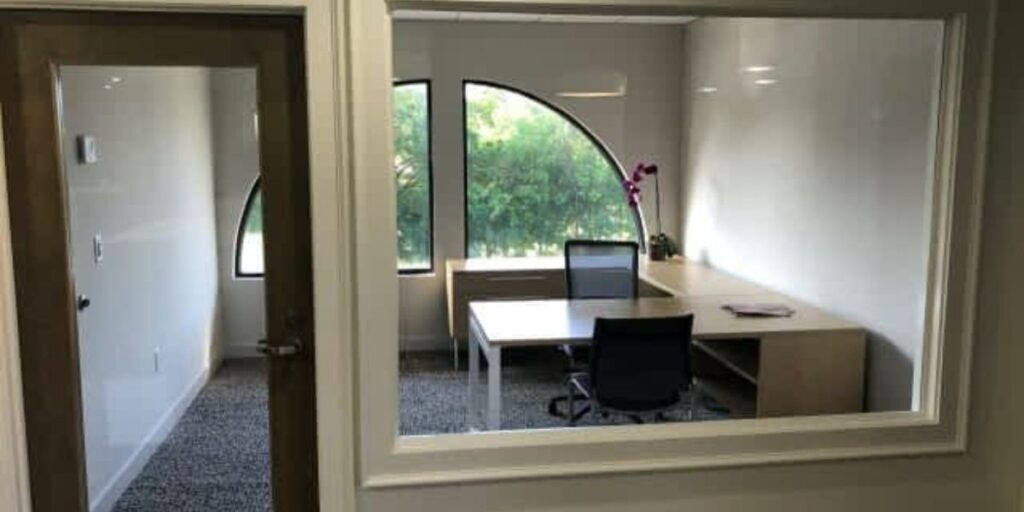 An office space with a desk, chair, and a large arch window overlooking greenery outside.