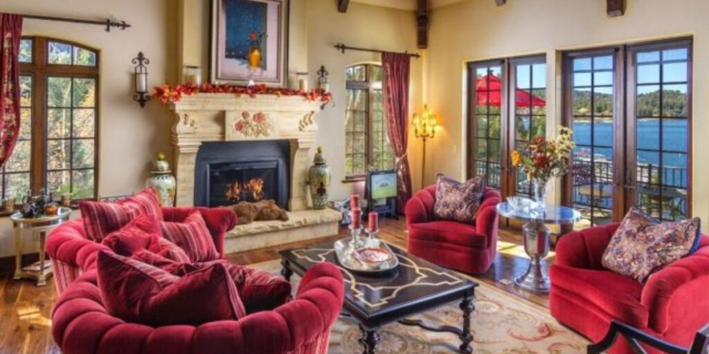 Cozy living room interior with a fireplace, plush red sofas, and a lake view through large windows.
