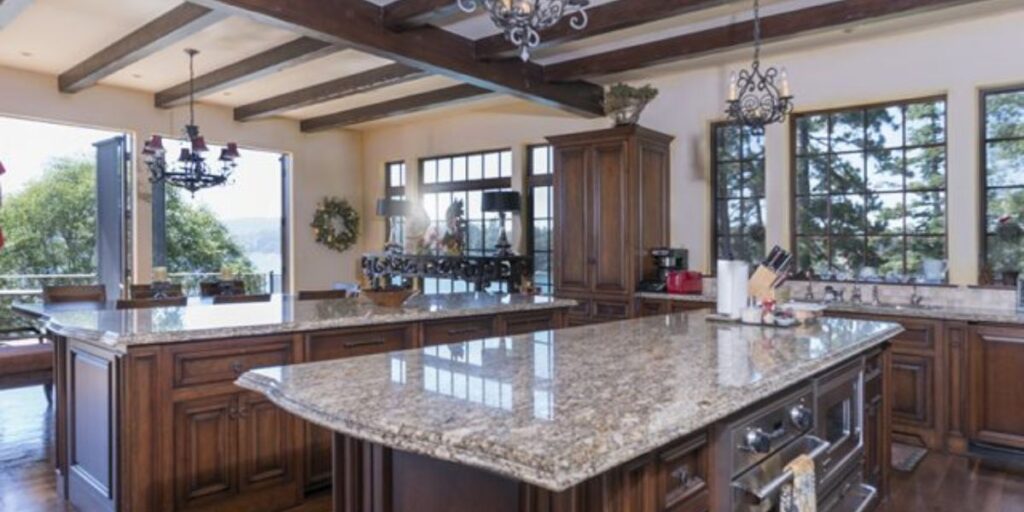 Spacious kitchen with a large granite island and rich wooden cabinetry, with a view of the outdoors.