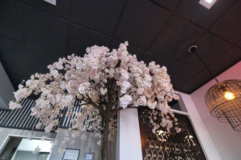 Indoor cherry blossom tree reaching up to a dark ceiling in a modern setting.