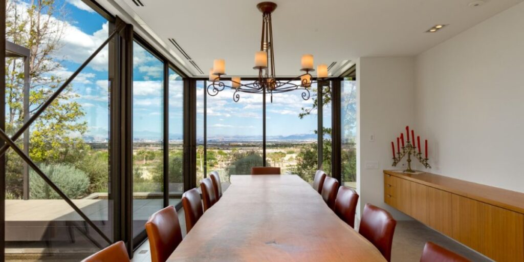 Spacious dining room with a long wooden table, leather chairs, and floor-to-ceiling windows overlooking a desert landscape.