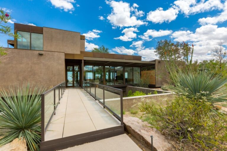 Exterior of a modern desert home with large windows and native landscaping.