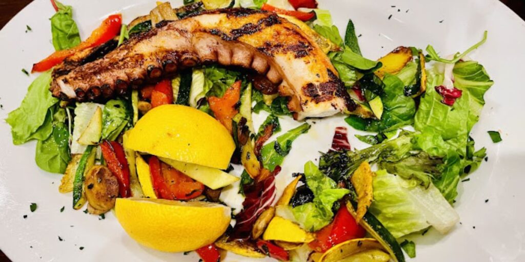 Grilled octopus over a bed of greens with lemon and grilled vegetables.