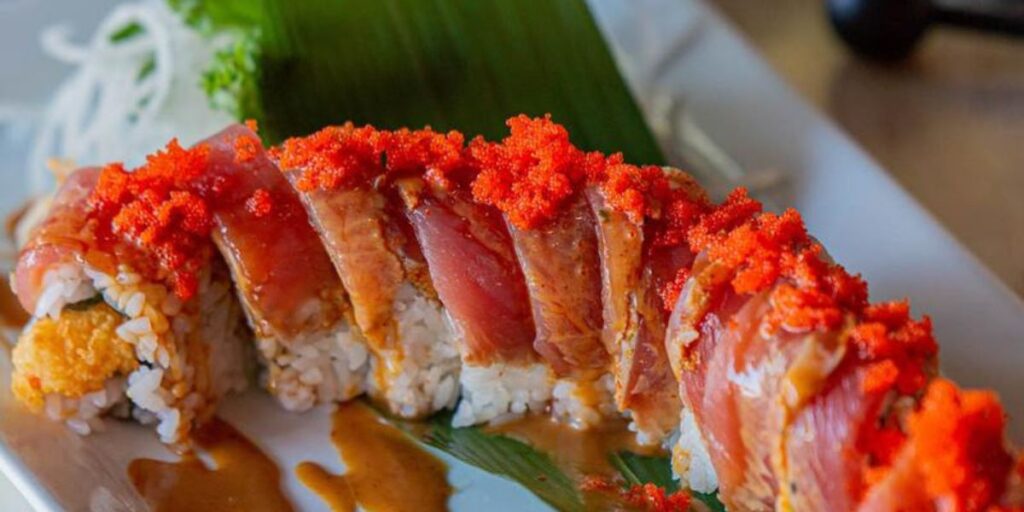 A delectable sushi roll topped with spicy roe on a white ceramic plate.