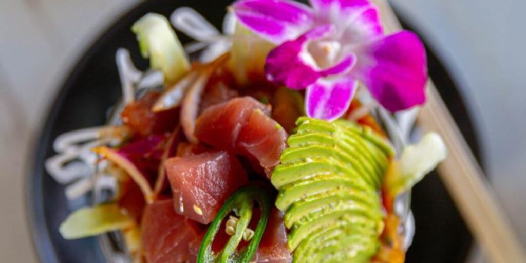 A beautifully presented poke bowl with tuna, avocado, and a floral garnish.