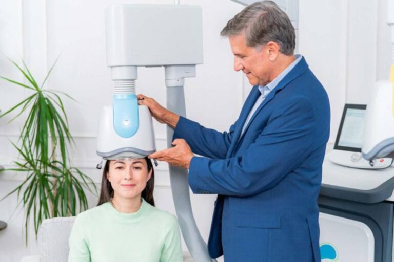 A woman receiving a transcranial magnetic stimulation (TMS) treatment with a medical professional adjusting the equipment.