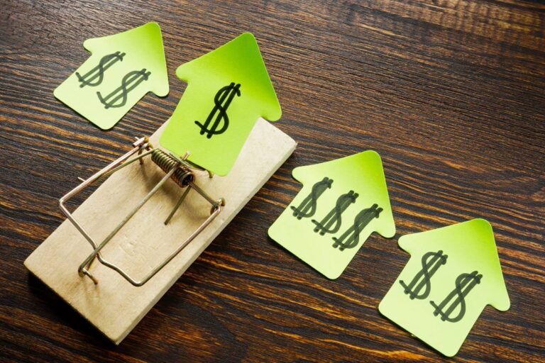 Mouse trap with dollar signs bait on green house-shaped sticky notes symbolizing financial traps in real estate.