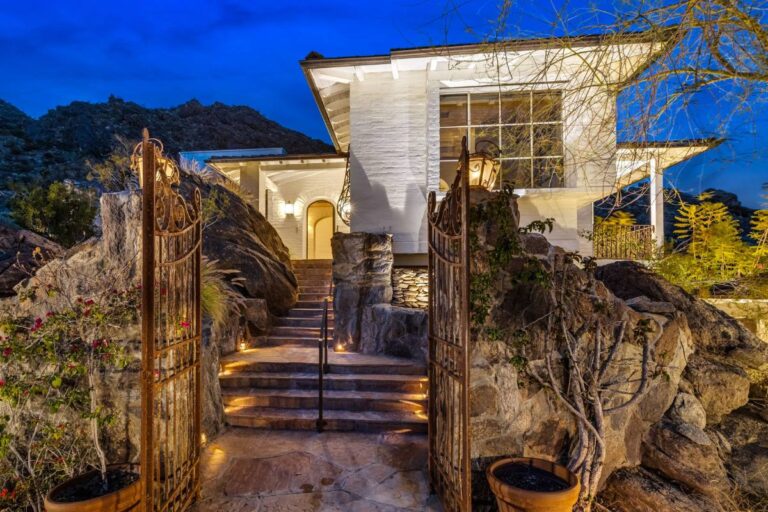 An elegant Palm Springs home nestled in a mountain setting at dusk, with lit pathway and ornate gates.