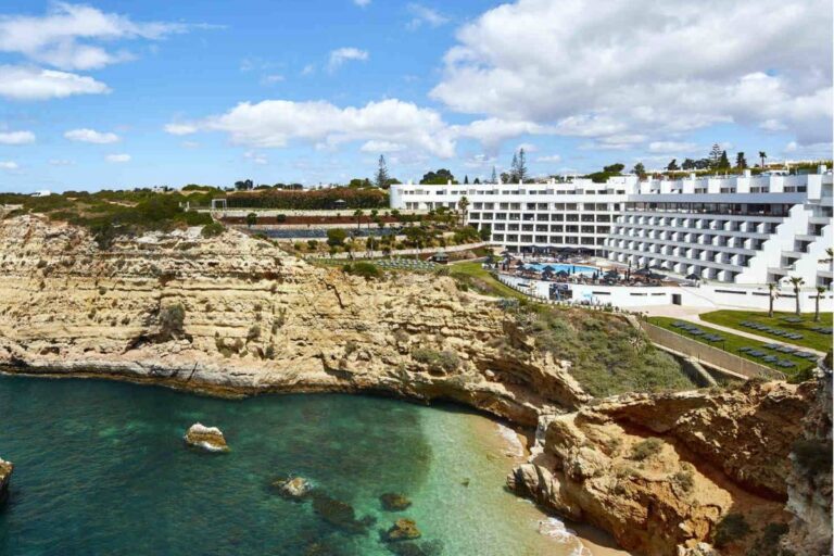 A luxury resort with white buildings overlooking a secluded cove with turquoise waters on the Algarve coast.