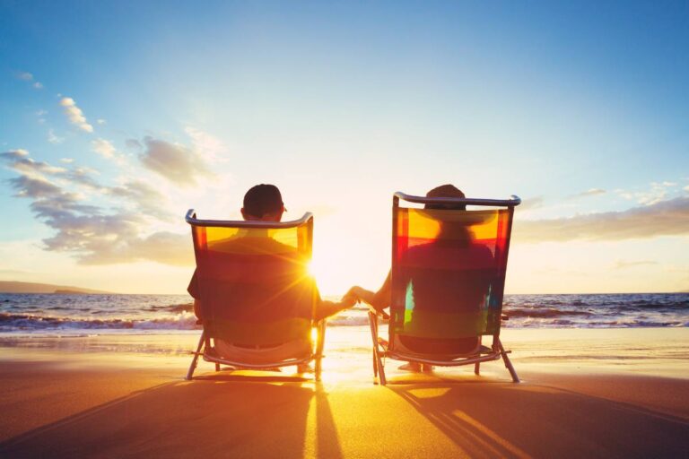 Two people sitting in beach chairs holding hands while watching the sunset over the ocean.