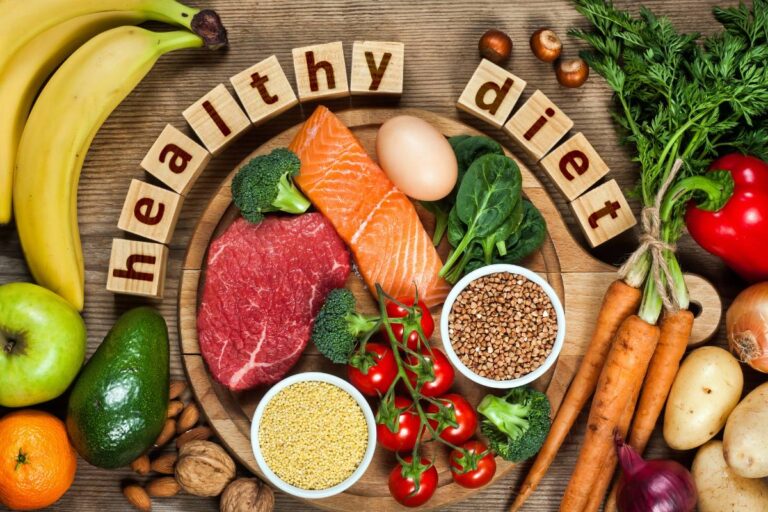 Assorted healthy foods including fruits, vegetables, nuts, grains, and protein sources artfully arranged around wooden blocks spelling out 'healthy diet.'