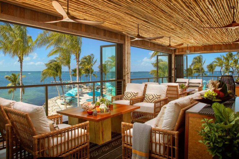 A cozy beachfront patio with rattan furniture and a view of palm trees and the ocean.