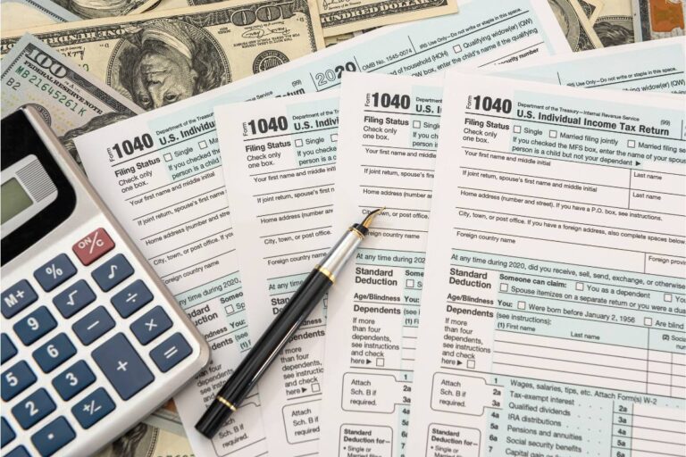 An assortment of U.S. Individual Income Tax Return forms, a calculator, a pen, and American currency spread out on a table.