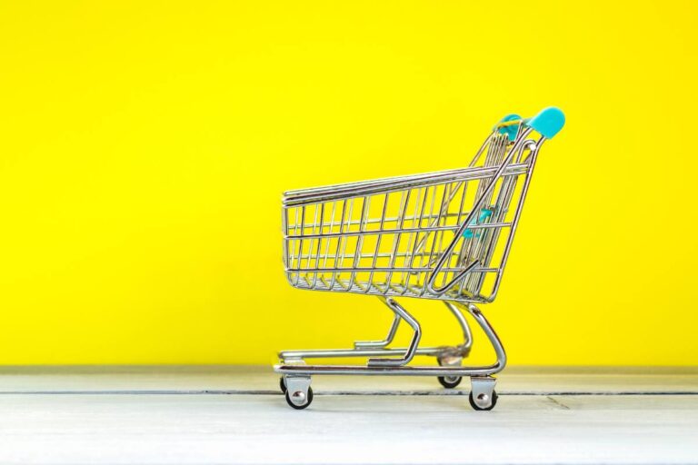 An empty mini shopping cart on a white surface against a bright yellow background.