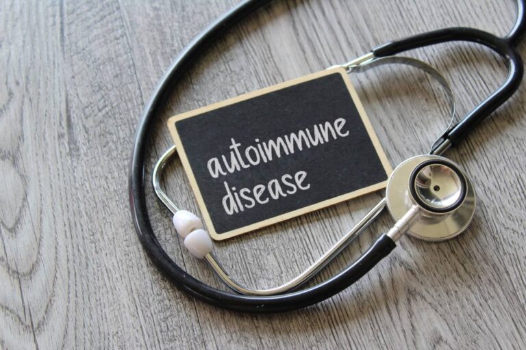 A stethoscope and a small chalkboard with "autoimmune disease" written on it, resting on a wooden surface.