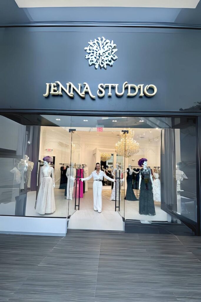 The entrance of JENNA STUDIO, with a woman greeting from the doorway and mannequins dressed in designer gowns.