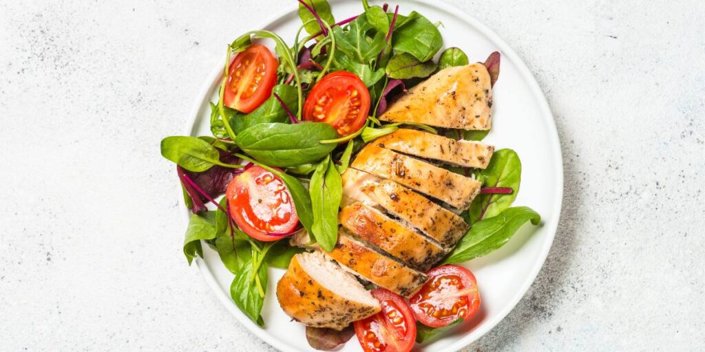 Sliced grilled chicken breast resting on a bed of mixed leafy greens and cherry tomatoes.