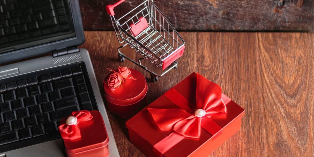 Red velvet gift boxes next to a laptop and a miniature shopping cart, representing online shopping.
