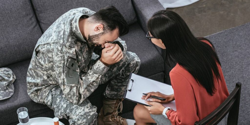 A distressed soldier in uniform during a therapy session with a female counselor taking notes.