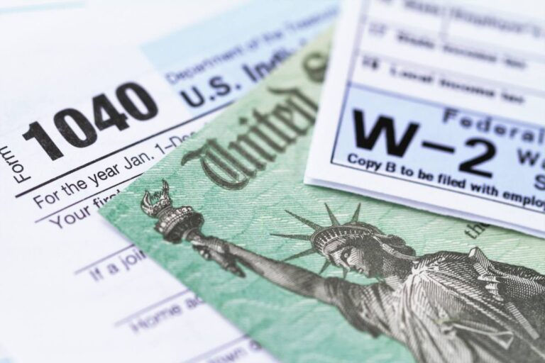 Close-up of U.S. tax forms, including the 1040 form and W-2 statement, with a part of a U.S. dollar bill visible.