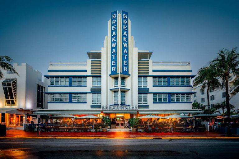 Twilight view of the iconic Art Deco Breakwater Hotel in Miami Beach with glowing neon signs
